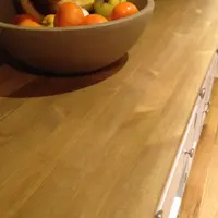 Close view across the oiled timber top, showing the open grain and knots beside a stoneware bowl of oranges and bananas, with round knobs on the drawer fronts at the edge