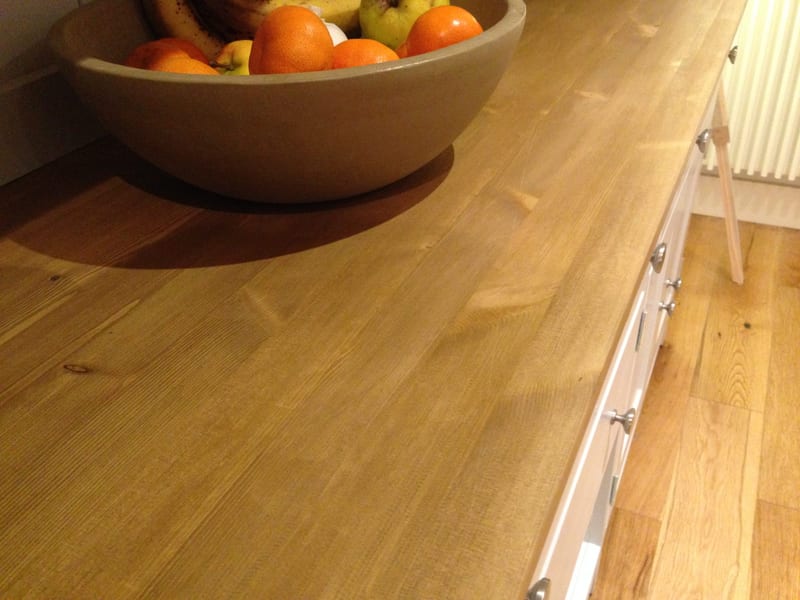 Close view across the oiled timber top, showing the open grain and knots beside a stoneware bowl of oranges and bananas, with round knobs on the drawer fronts at the edge