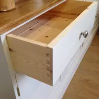 Detail of a drawer pulled out of the dresser base, showing the natural solid pine drawer box, hand-cut dovetail joints and a brushed nickel knob on the painted front