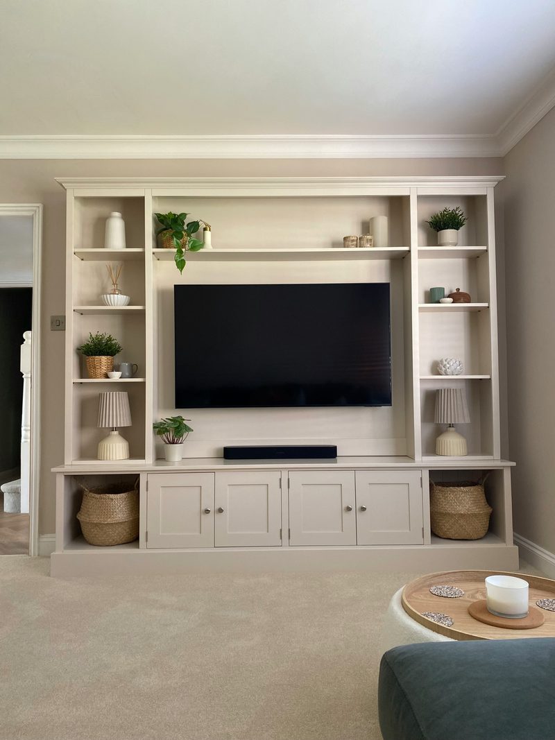 Stone painted 8ft Milton media wall with a large wall mounted television, tall open shelf columns holding lamps, plants and ceramics, and cupboards with seagrass baskets along the base