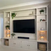 Angled view of the media wall from the right, showing the deep cornice, the recessed television panel, the soundbar shelf and the cupboards with brushed nickel knobs above the plinth