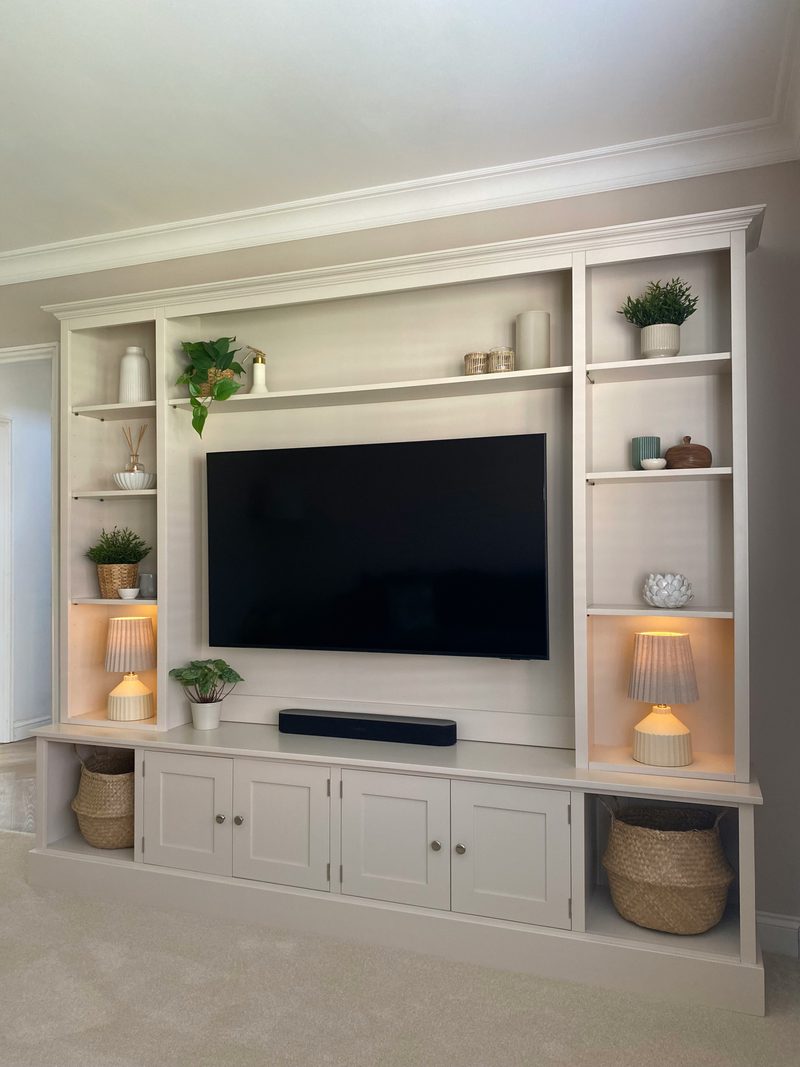 Angled view of the media wall from the right, showing the deep cornice, the recessed television panel, the soundbar shelf and the cupboards with brushed nickel knobs above the plinth