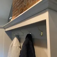 Detail of the cornice above the coat rail, showing a row of antique brass double hooks on the tongue and groove backboard with a cream jacket and a navy quilted coat hanging