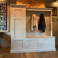 Straight-on view of the whole boot room unit against a sage panelled wall, with a framed bus blind print to one side and white fish-shaped and green plates displayed on the wall to the other