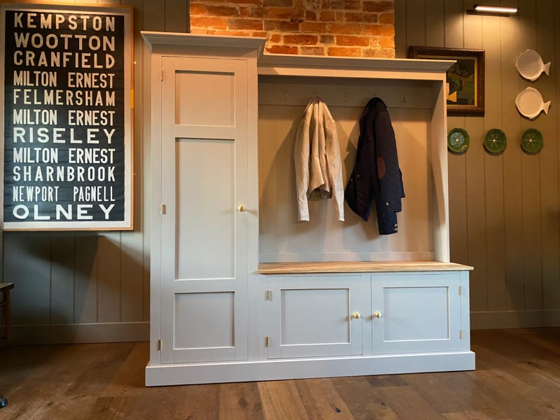 Straight-on view of the whole boot room unit against a sage panelled wall, with a framed bus blind print to one side and white fish-shaped and green plates displayed on the wall to the other