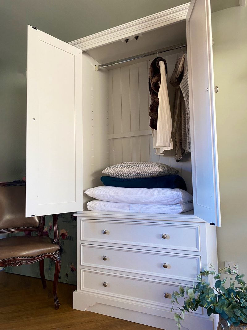 Cream painted Carlton double wardrobe with both doors opened to show a hanging rail with clothes and folded bedding on the shelf, above three drawers in the base