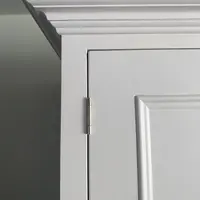 Detail of the top corner of the white painted wardrobe, showing the stepped moulded cornice, a brushed nickel butt hinge and the raised panel edge of the door