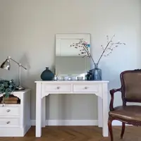 Portrait view of the dressing table styled with a bevelled mirror, dark ceramic vase, reed diffuser and three small white bowls, beside a bedside cabinet and a leather armchair