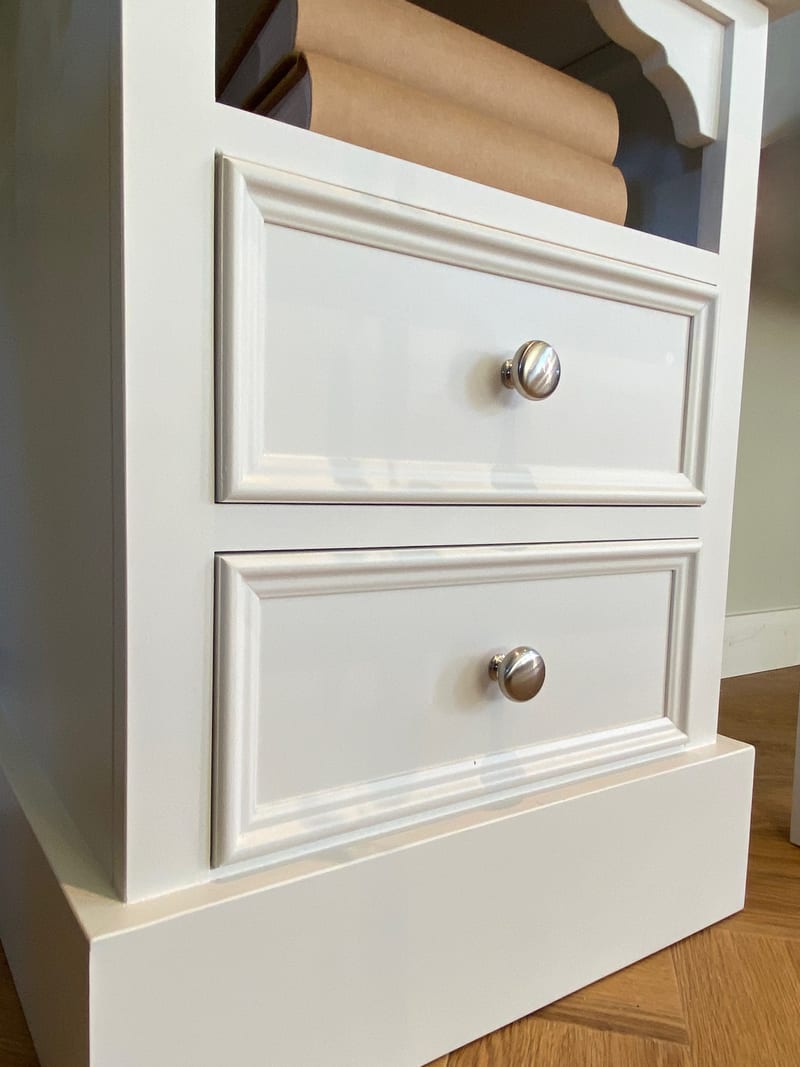 Close view of the two moulded drawer fronts of the white painted bedside cabinet, showing the round brushed nickel knobs, the crisp paint finish and the stepped plinth base beneath