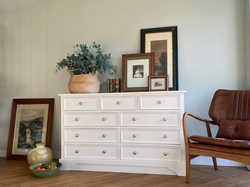 Cream painted Carlton large chest with three short drawers above three pairs of long drawers, styled with eucalyptus, books and framed prints beside a tan leather chair