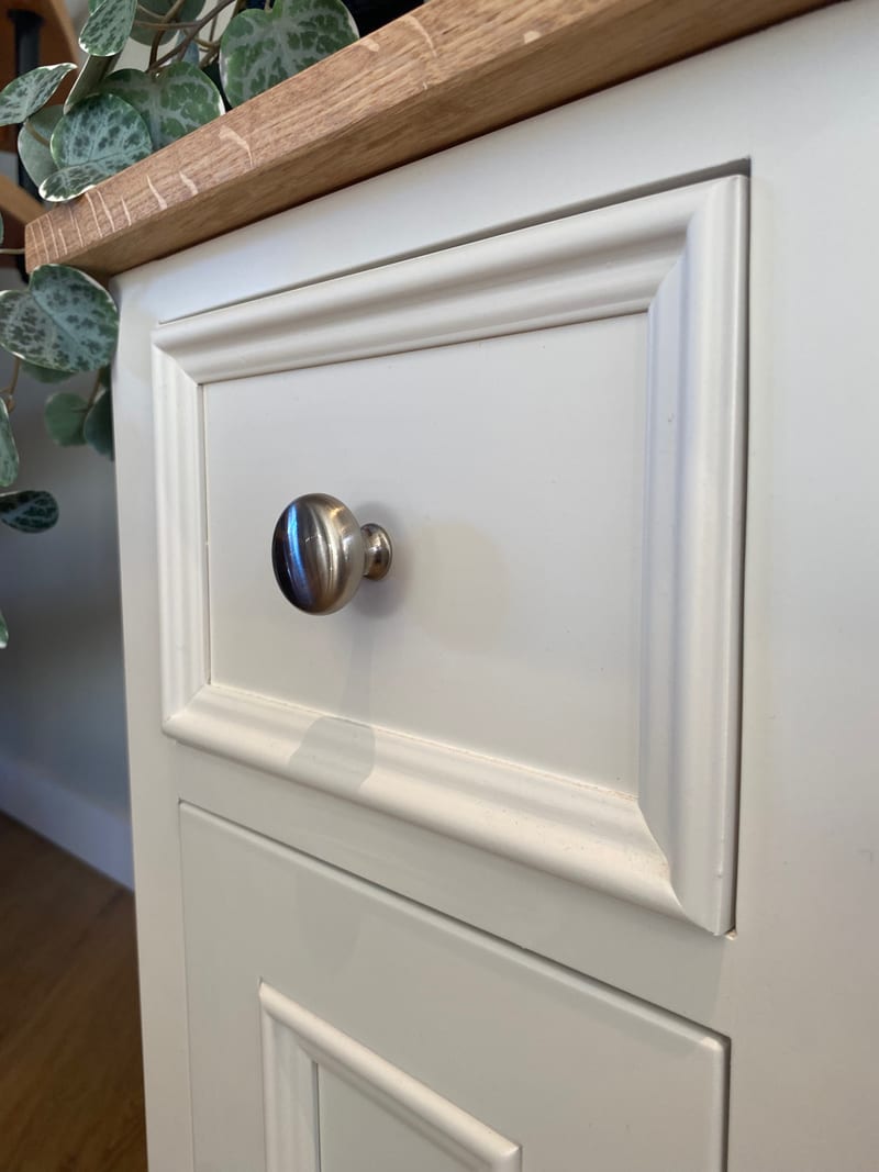 Close view of the top drawer front, showing the layered moulding, the brushed nickel knob and the sawn edge of the oak top with trailing foliage resting above it