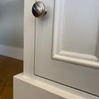 Detail of the panelled door and its round brushed nickel knob, with the moulded frame and the top edge of the painted plinth catching the light against a pale grey wall