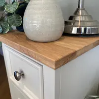 Close view of the corner of the solid oak top, showing the grain and sawn edge beside a crackle glazed cream vase and the polished nickel base of a table lamp