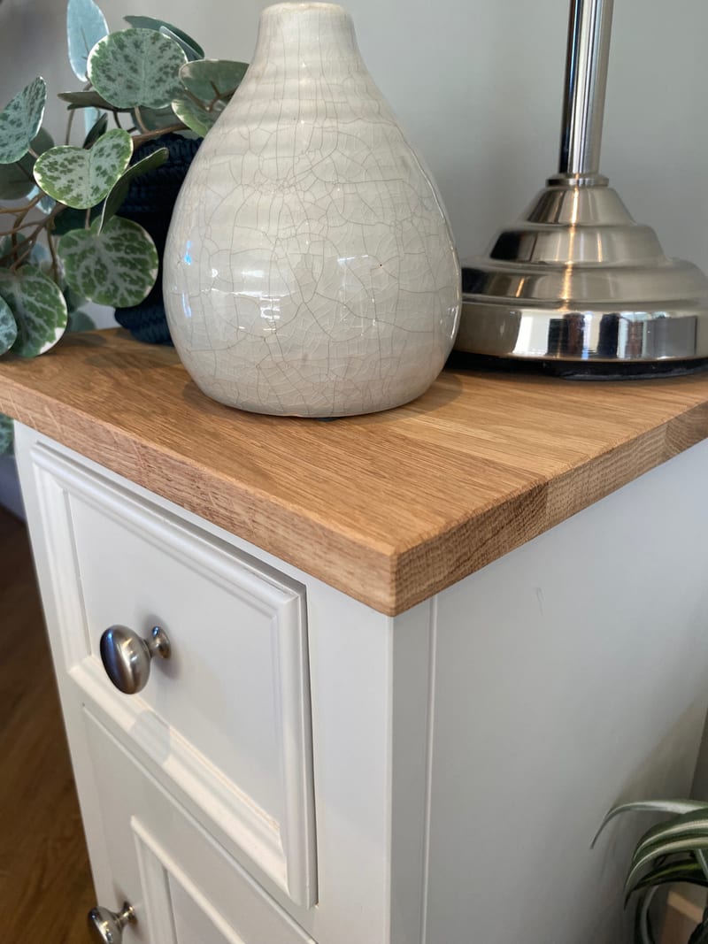 Close view of the corner of the solid oak top, showing the grain and sawn edge beside a crackle glazed cream vase and the polished nickel base of a table lamp