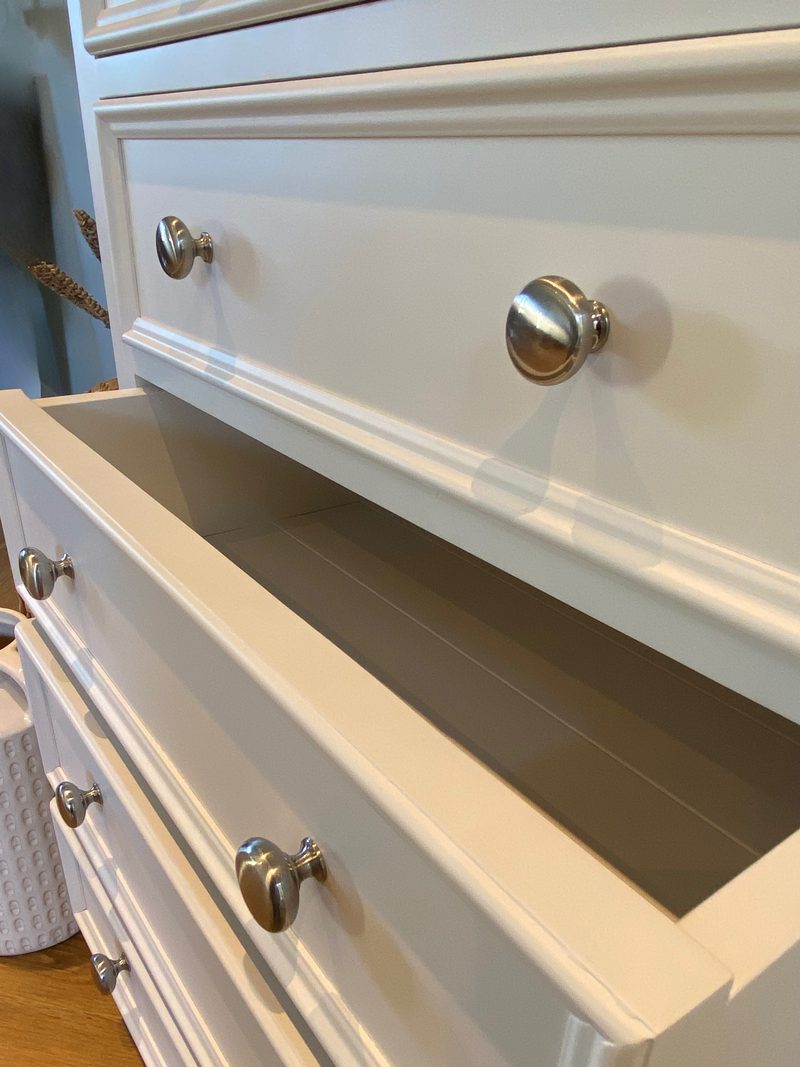 Close view of one drawer pulled open, showing the smooth painted interior of the drawer box and the moulded fronts and round nickel knobs of the drawers above and below
