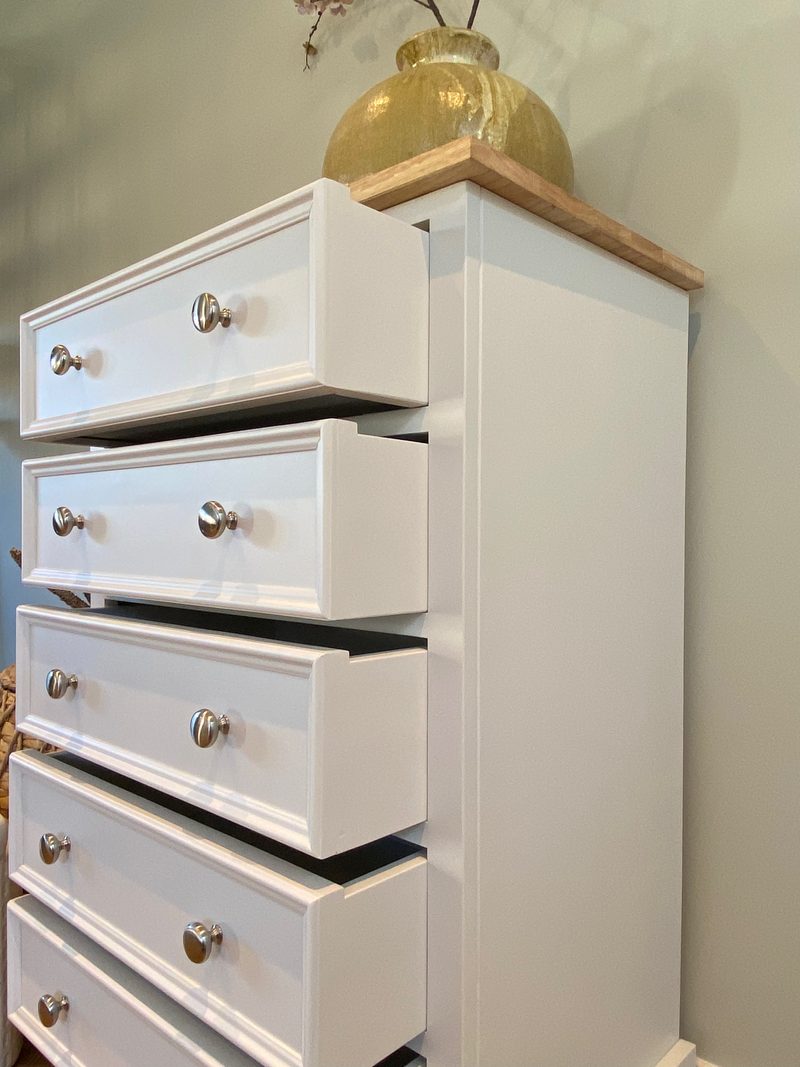 Angled view from the side with the drawers stepped open, showing the depth of the painted drawer boxes, the plain painted side panel and the oak top with a glazed olive vase