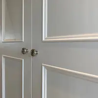 Close detail of two doors meeting, showing the pair of round brushed nickel knobs and the crisp bevelled mouldings that frame the recessed painted panels