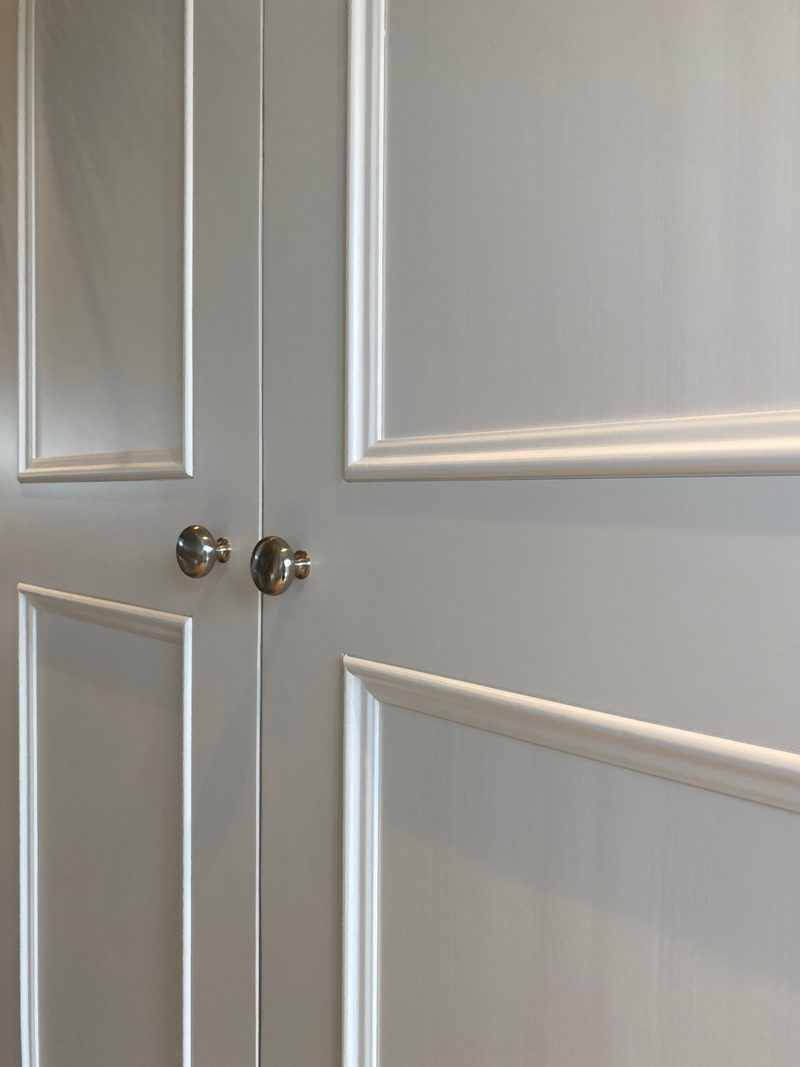 Close detail of two doors meeting, showing the pair of round brushed nickel knobs and the crisp bevelled mouldings that frame the recessed painted panels