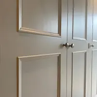 View along the front of the wardrobe at an angle, showing the tall panelled doors, the narrow shadow gaps between them and three round nickel knobs, a pair where two doors meet and one beyond