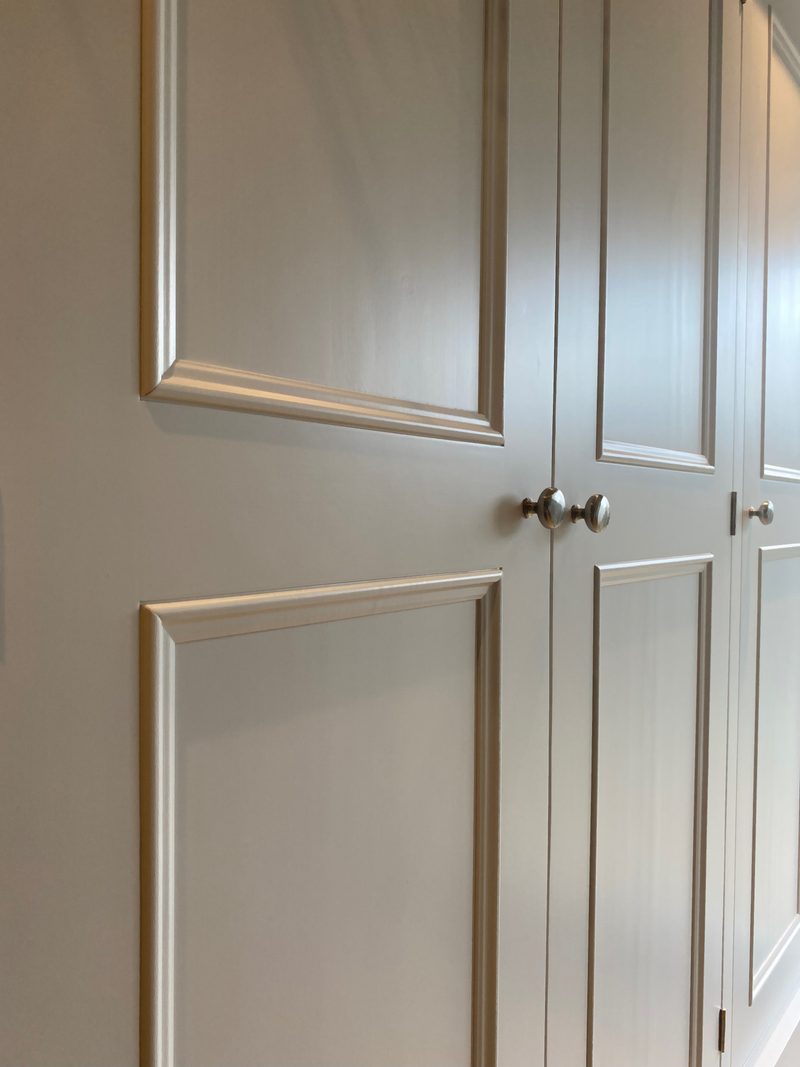 View along the front of the wardrobe at an angle, showing the tall panelled doors, the narrow shadow gaps between them and three round nickel knobs, a pair where two doors meet and one beyond