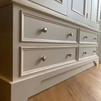 Angled view of the four base drawers beneath the panelled doors, showing the moulded fronts, paired round nickel knobs and the shaped plinth standing on oak flooring