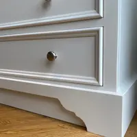 Close corner detail of two stacked drawers and the shaped bracket plinth, showing the moulded drawer frames, the round nickel knob on each front and the light oak floor below