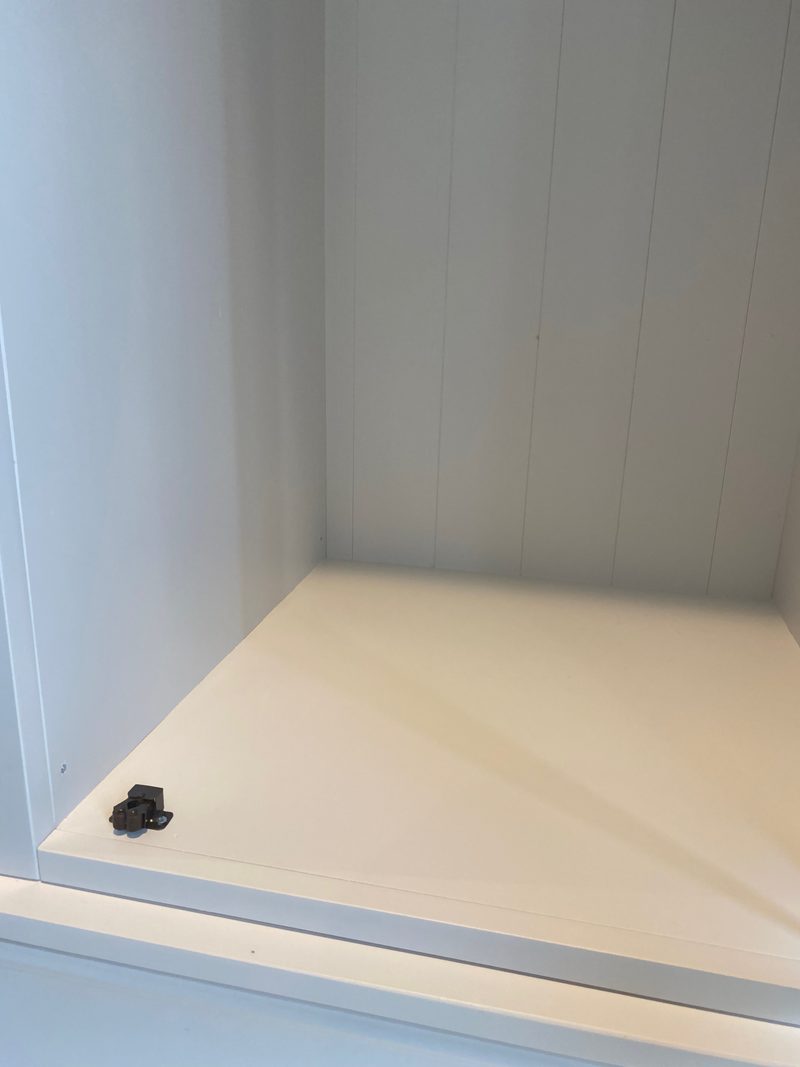 Inside the base of the wardrobe, showing the painted floor board, the tongue-and-groove back panelling and a small dark door catch fixed near the front edge