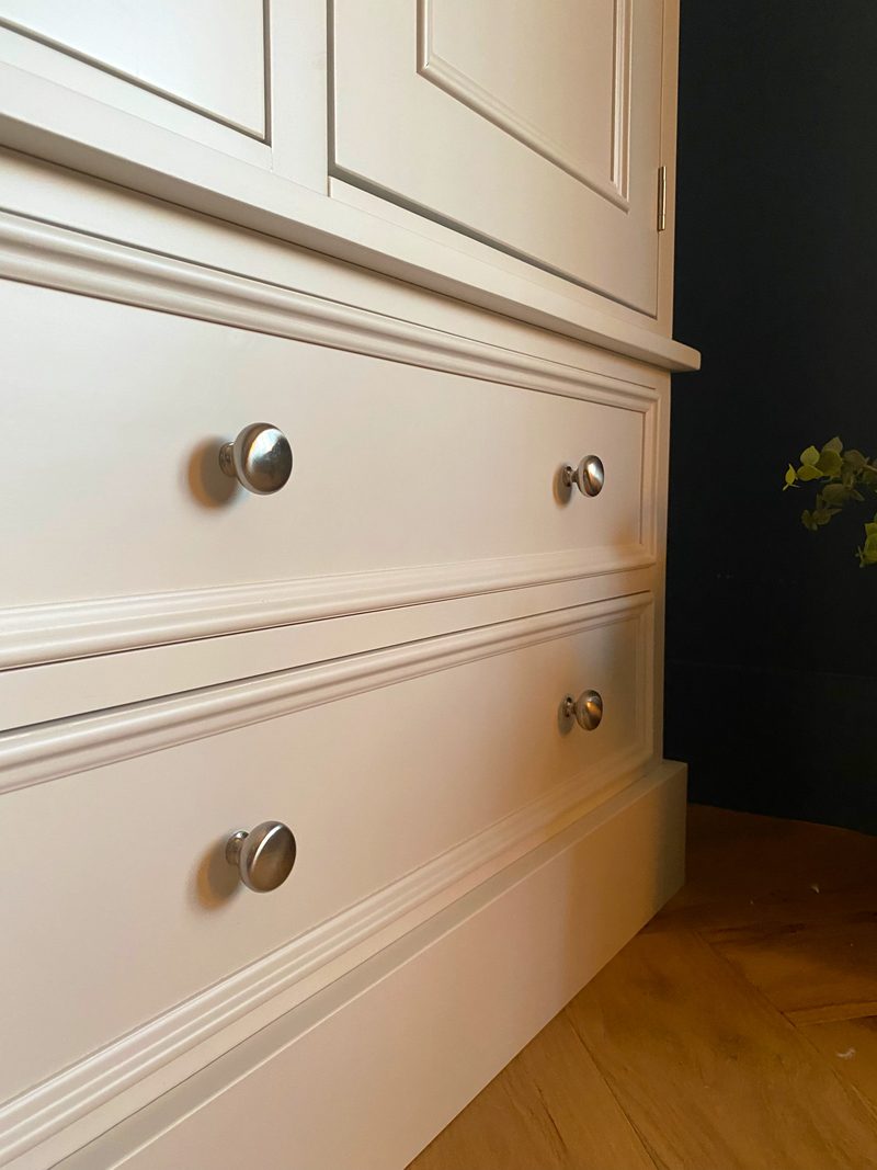 Side-on detail of the lower drawer fronts, showing the beaded drawer surrounds, a pair of brushed nickel knobs on each drawer and the deep moulded plinth above oak flooring