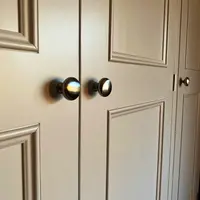 Close view of the meeting point of two panelled wardrobe doors, showing a pair of round brushed nickel knobs, the moulded panel edges and a third door knob further along the front