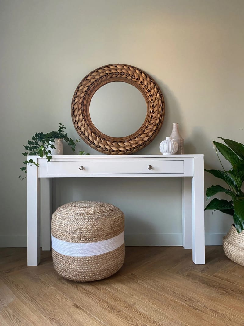 White painted Colmworth console table with a single long drawer on square tapered legs, beneath a round rattan mirror with a jute pouffe tucked underneath