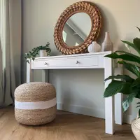Angled landscape view of the console table beside sage green curtains, showing the straight square legs, the long single drawer with two nickel knobs and a jute pouffe tucked underneath