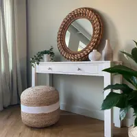 Portrait view of the console table against a soft green wall, with linen curtains to one side, a peace lily to the other and a striped jute pouffe on the herringbone wood floor