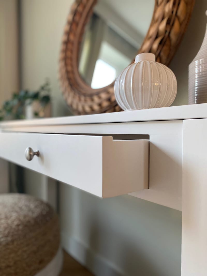 Detail of the drawer eased open, showing the thickness of the painted drawer front, the smooth painted drawer side and the single round brushed nickel knob on the white table