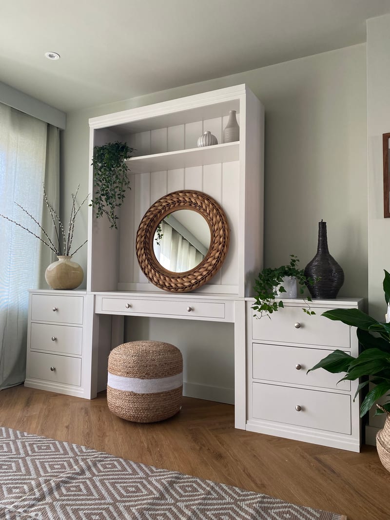 White painted Colmworth modular dressing table with a canopy shelf above a round rattan mirror, flanked by two three drawer chests, with a jute pouffe tucked underneath