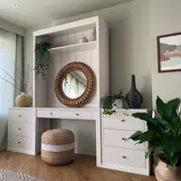 Angled view of the painted dressing table with its open display shelf, tongue-and-groove back panel and round woven rattan mirror, set between two flanking three-drawer chests
