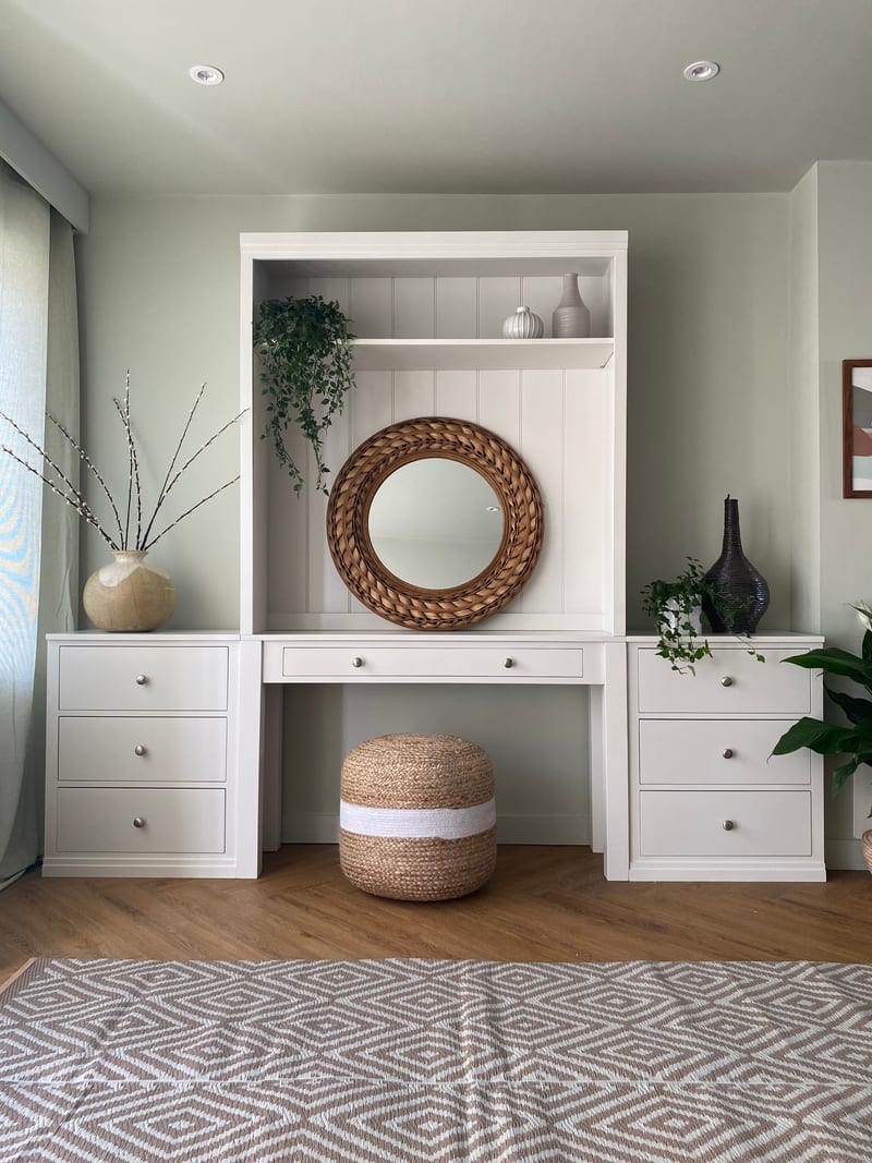 Straight-on view of the dressing table and shelved top between two matching three-drawer chests, with a jute pouffe beneath and a diamond-patterned rug across the wood floor