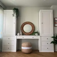 White painted Colmworth dressing table between two tall cupboards over three drawer chests, with a round rattan mirror above and a jute pouffe beneath