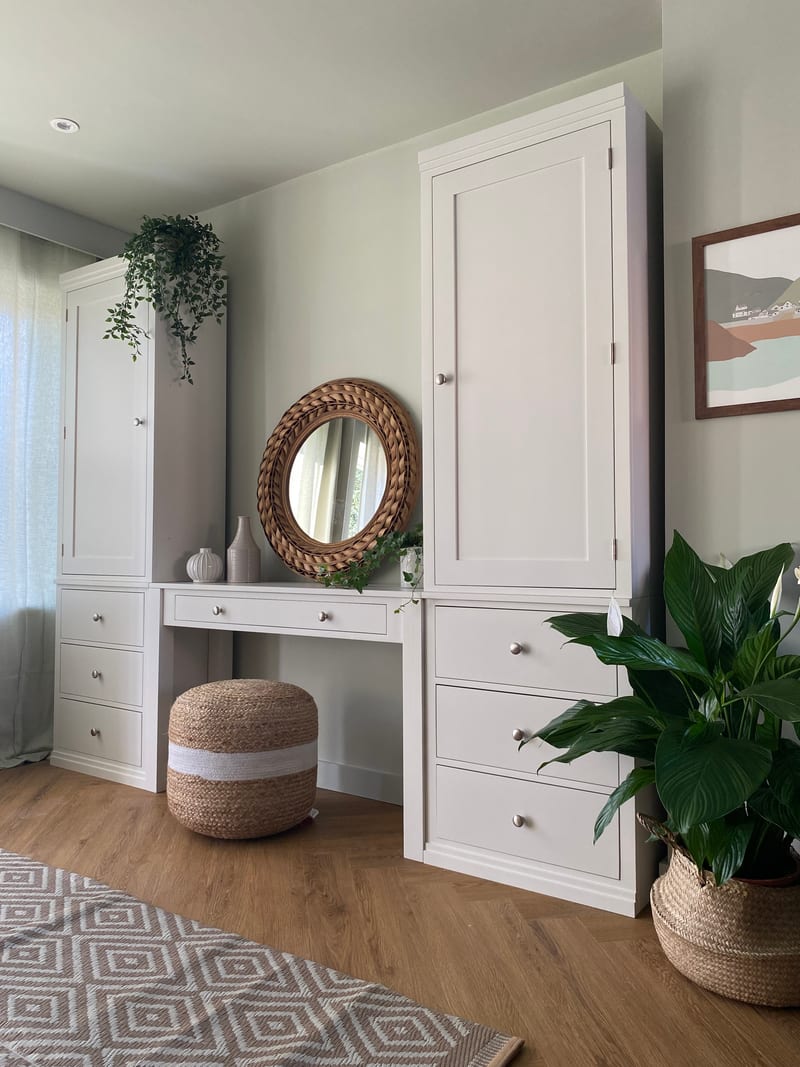 Angled view along the run with the right-hand tall single-door cupboard in the foreground, each cupboard standing over three drawers, beside a framed coastal print and a large peace lily
