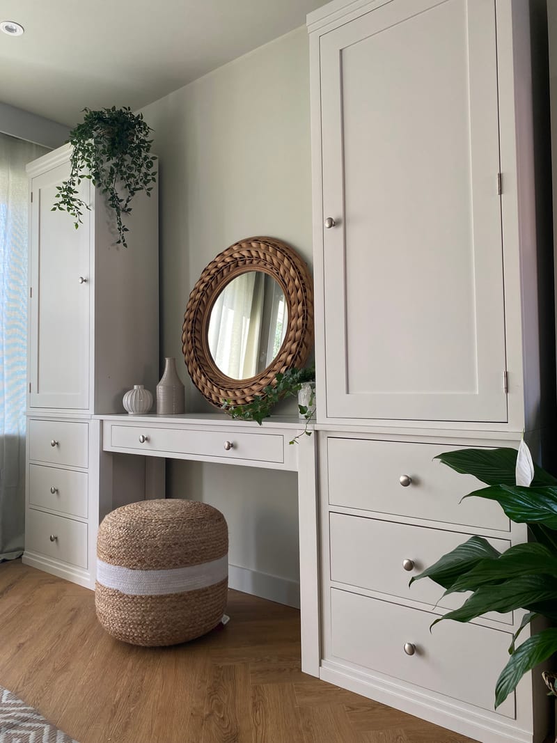 Close angled view of the right-hand tall cupboard, showing its recessed panelled door, brushed nickel knobs and three deep drawers beside the desk and its woven jute pouffe