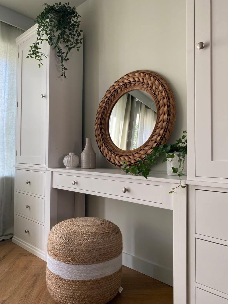 Close view of the dressing table top with the round woven rattan mirror, two ribbed stoneware vases, a trailing ivy and the single wide drawer with two brushed nickel knobs