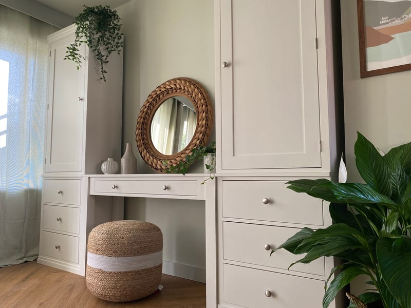 Landscape view across the run with an artificial trailing plant on the left cupboard top, the rattan mirror and vases on the desk and three drawers under the right cupboard