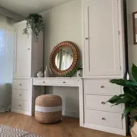 Wide landscape view of the dressing table lit by a sunlit curtained window on the left, with the jute pouffe tucked under the desk and a peace lily in a woven basket at the right