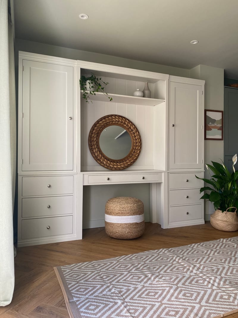 White painted Colmworth dressing table wall with a mirrored recess and display shelf between two tall cupboards over drawers, with a jute pouffe beneath the drawer