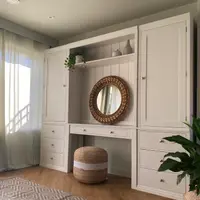 Landscape three-quarter view of the built-in dressing table between two tall cupboards, with sunlight through sage linen curtains on the left and a peace lily on the right
