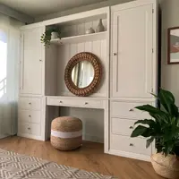 Angled view of the whole unit showing the central dressing table recess, the moulded top shelf holding vases and an ivy, and a diamond-patterned rug on the wood-effect floor