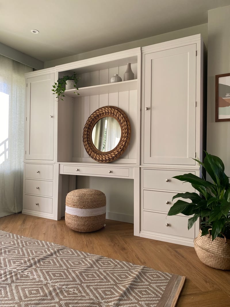 Angled view of the whole unit showing the central dressing table recess, the moulded top shelf holding vases and an ivy, and a diamond-patterned rug on the wood-effect floor