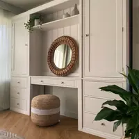 Closer angled view of the right-hand tall cupboard door and the three drawers beneath it, with the recessed dressing table, round rattan mirror and jute pouffe to the left