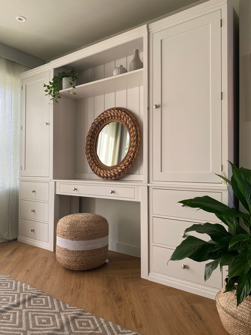 Closer angled view of the right-hand tall cupboard door and the three drawers beneath it, with the recessed dressing table, round rattan mirror and jute pouffe to the left