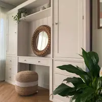 Angled view along the run with a peace lily filling the right foreground, showing the desk drawer with two knobs, the open kneehole and the stacked drawers beneath each tall cupboard