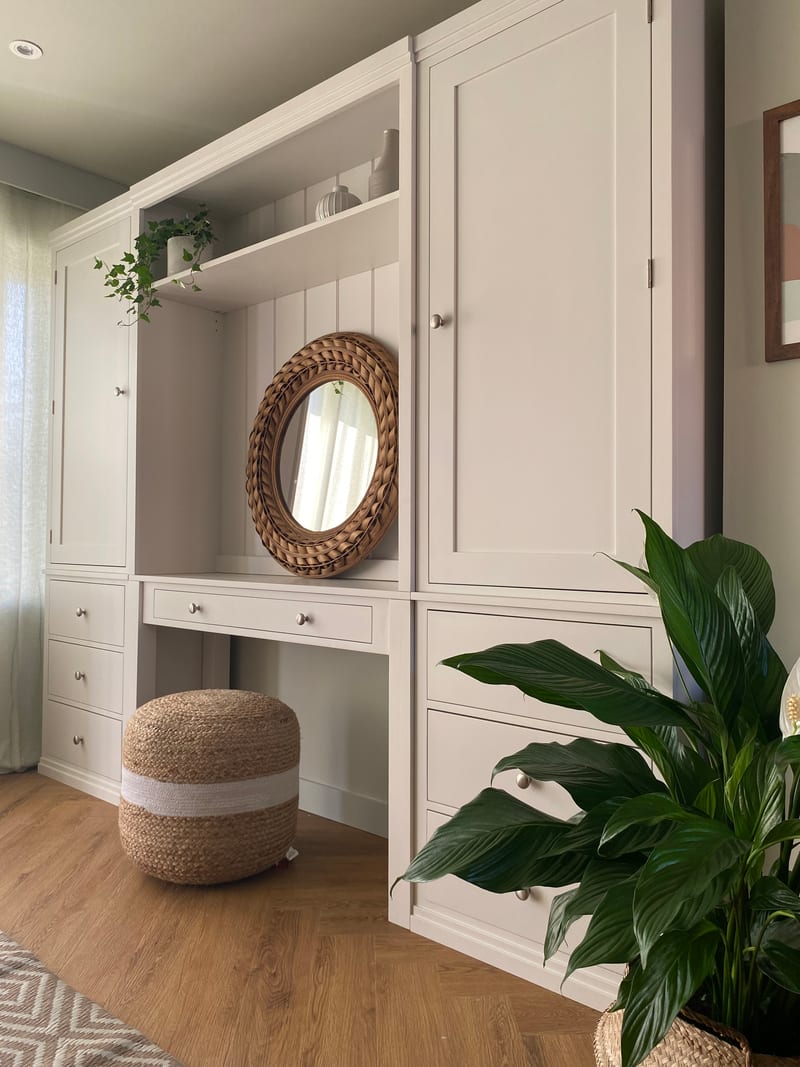 Angled view along the run with a peace lily filling the right foreground, showing the desk drawer with two knobs, the open kneehole and the stacked drawers beneath each tall cupboard